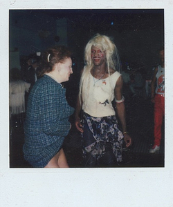 A Photograph of Marsha P. Johnson with Blonde Hair, White Top, and Black and Pink Patterned Skirt, Dancing with Another Person