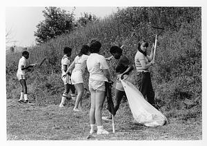 Group of unidentified young people clearing a field of grass