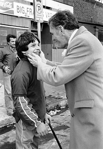 Mayor Raymond L. Flynn holding face of an unidentified boy in front of variety store