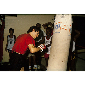 Man preparing to hit a punching bag, while young boys look on