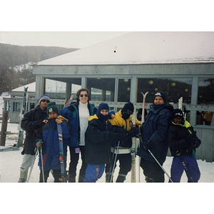 Woman and six boys posing with their skis in front of a ski lodge.