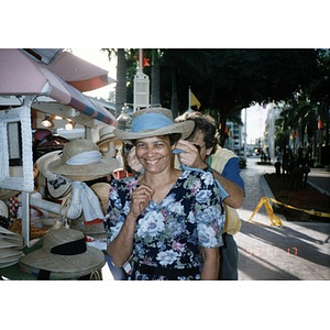 Woman trying on a hat outside at a vendor's cart.