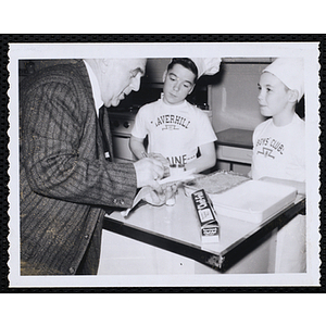 Two members of the Tom Pappas Chefs' Club consult with an unidentified man in kitchen