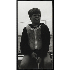 A boy sits on the deck of sailboat on Boston Harbor