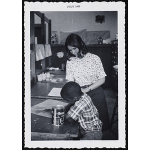 A seated boy draws on a paper as a woman looks on during Tom Sawyer Day