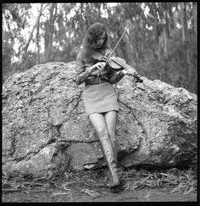 Woman playing a fiddle, posed on a granite boulder in a eucalyptus grove