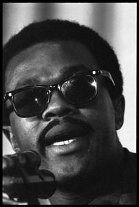 Bobby Seale: close-up portrait, speaking at a podium, wearing sunglasses