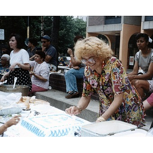 Woman preparing to cut a sheet cake during an outdoor community celebration.
