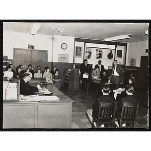 An unidentified man addresses a group of boys and teenagers in a library