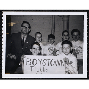 An unidentified man poses with boys holding a Boystown poster