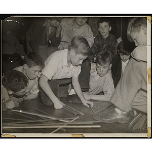 A Large group of boys playing a game of pick up sticks on the floor