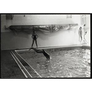 A girl dives into a natorium pool as another girl looks on