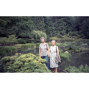 Two women stand in front of a pond in a park