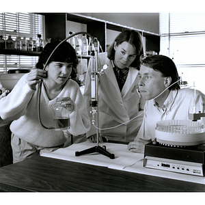 Two students examine an experiment while their professor observes them