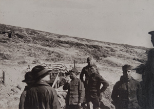 Red Cross workers and soldiers standing in front of a hillside dugout entrance