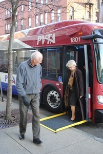 Congressman John W. Olver walking past a Pioneer Valley Transit Authority bus with woman descending an accessibility ramp