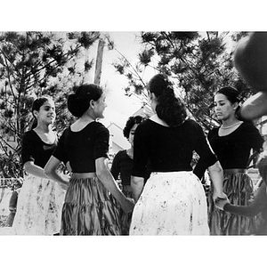 Young women dancing in a ring on an outdoor stage.