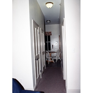 Looking down a narrow hallway towards a table and chairs in a furnished unit in Villa Victoria housing.