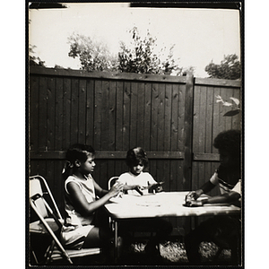 Three children play cards at a table outdoors