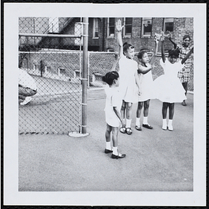 Girls standing in a semicircle and raising their hands during a Little Sister Contest
