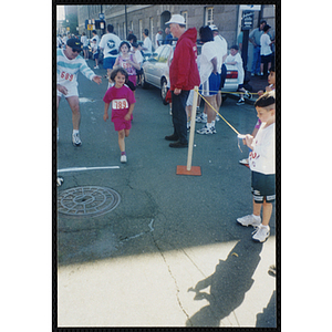 A girl is cheered on by a man as she runs in the Battle of Bunker Hill Road Race