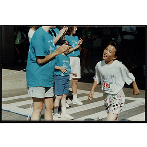 A girl passes the finish line as race officials cheer her on at the Battle of Bunker Hill Road Race