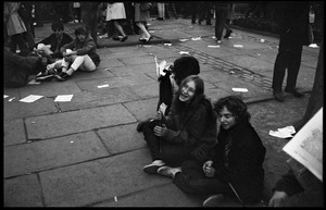 Three young women sit on the sidewalk, observing the Moratorium protests