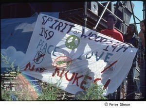 MUSE concert and rally: MUSE staff member holding banner in front of rally stage that reads, 'spirit of woods, peace love, no nukes'