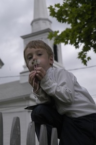 Church supper at the First Congregational Church, Whately: boy blowing on the seed head of a dandelion in front of the church