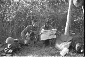 G.I.'s reading the Stars and Stripes in the field.